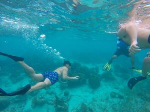 Man snorkeling in Belize under about 7 feet of clear blue water with bubbles rising, showing the cool and refreshing side of a Belize coolcation.