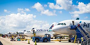 Travelers disembarking on the tarmac under blue skies at Belize International Airport, with open airplane doors and ground crew assisting. (Flights to Belize)