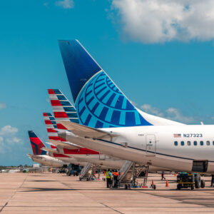 Airplanes on the tarmac at Philip Goldson International Airport in Belize City with Delta, American Airlines, and Continental tail fins as staff attend the boarding stairs.