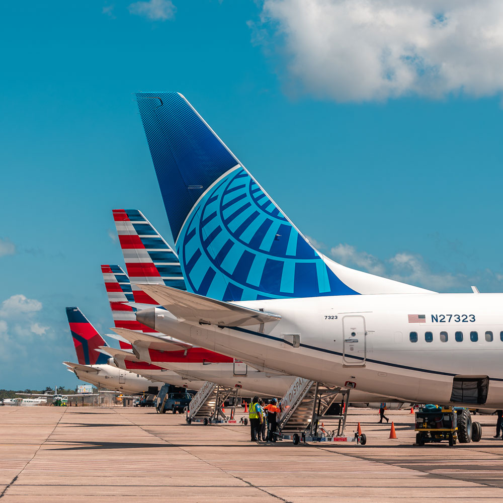 Airplanes on the tarmac at Philip Goldson International Airport in Belize City with Delta, American Airlines, and Continental tail fins as staff attend the boarding stairs.