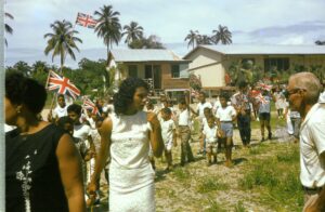 Children and adults in Placencia, Belize during Queen of the Bay Pageant, 1965–1967, with British flag during St. George’s Caye Day