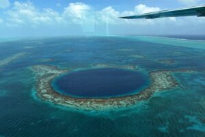 Aerial view of the Great Blue Hole Belize with plane wing in upper right during flyover tour.
