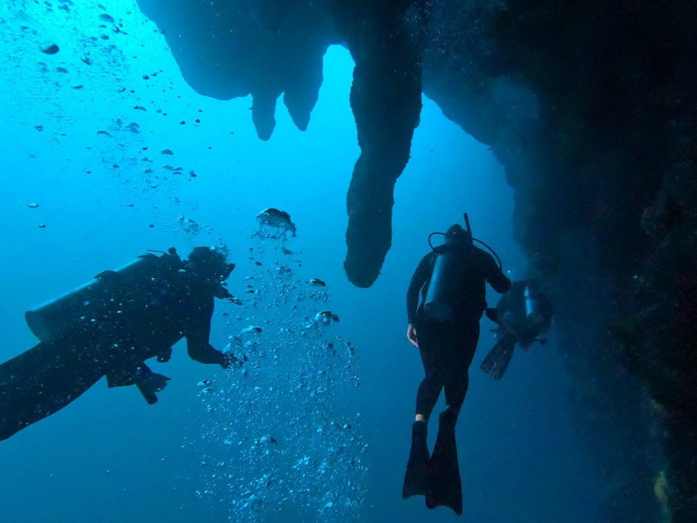 Three scuba divers exploring stalactites inside the Great Blue Hole in Belize