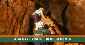 A licensed guide in the ATM Cave helps a woman climb to an upper chamber, holding a flashlight while she ascends the limestone rock passage in Belize.